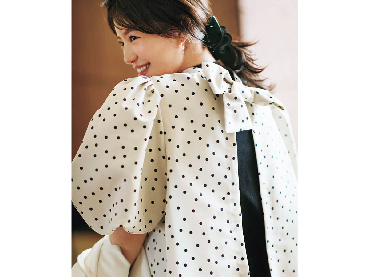 バックにリボンがついたアローのドット柄ブラウスを着た咲和希さん