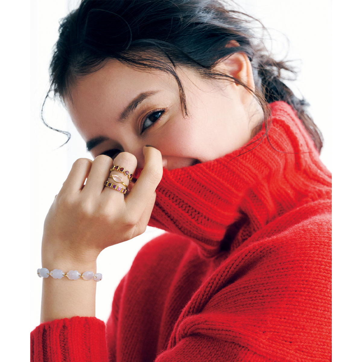 赤のタートルネックを着てマリーエレーヌドゥタイヤックのカラーストーンのブレスレットや指輪を重ねづけした岸本セシルさん