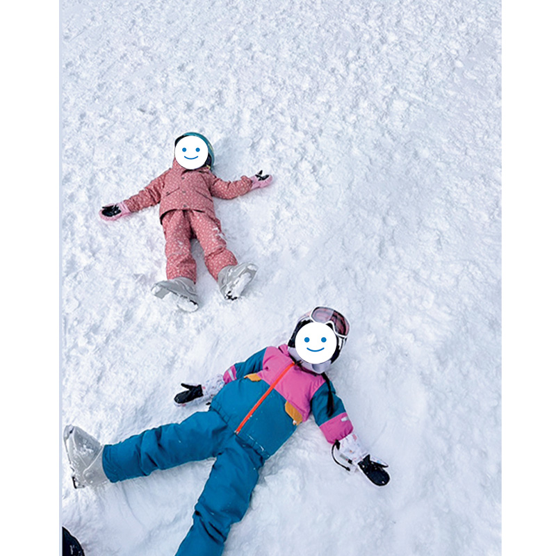 カラフルなスキーウェアを着て雪の上に寝転ぶ子どもたち