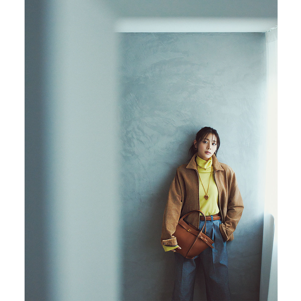 イエローのタートルニットとデニムにキャメルのアウターやバッグを合わせたコーデ