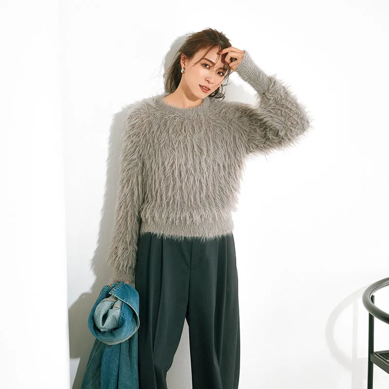 グレーのシャギーニットに黒パンツ、デニムジャケットを手に持ったコーデ