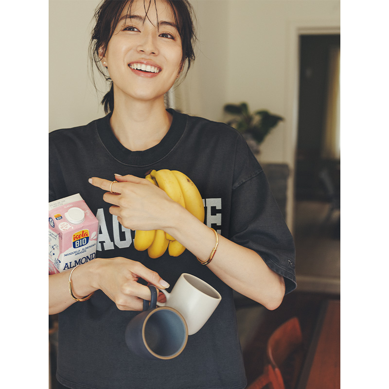 Tシャツ姿でバナナやマグカップを持つ手にティファニーロックのバングルとリングを身につけた笹川友里さん