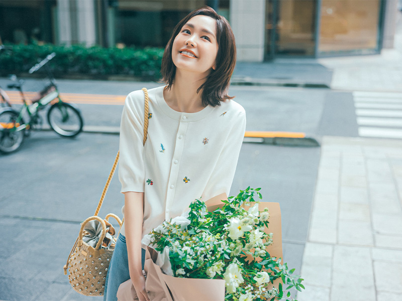 CABaNのボタニカル刺繍の半袖カーデとデニムにクリスタルのついたカゴバッグを肩にかけて花束を持った桐谷美玲さん