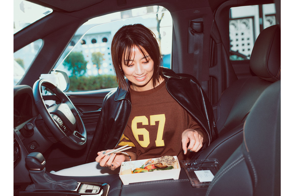 車の中でお弁当を食べているロゴスウェットを着た東原亜希さん