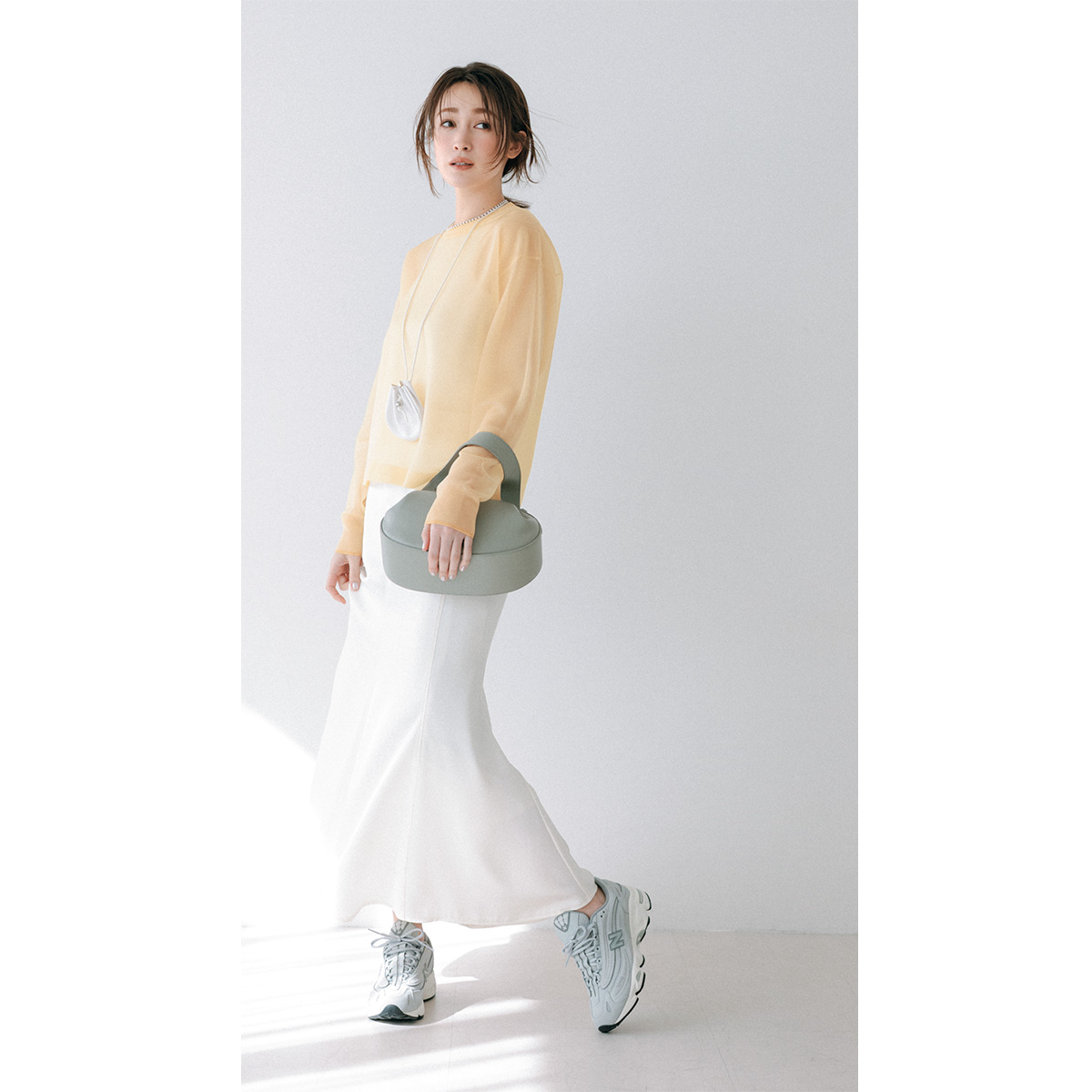 バターイエローのシアーニットに白の艶スカートのコーデ