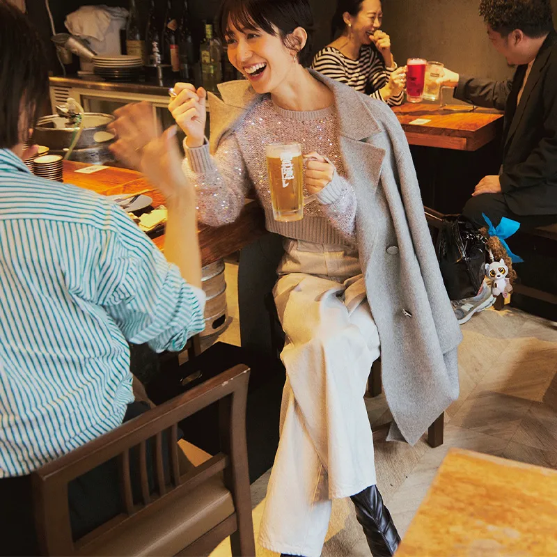 スパンコールニットに厚手のロングコート、ホワイト系のパンツのコーデ